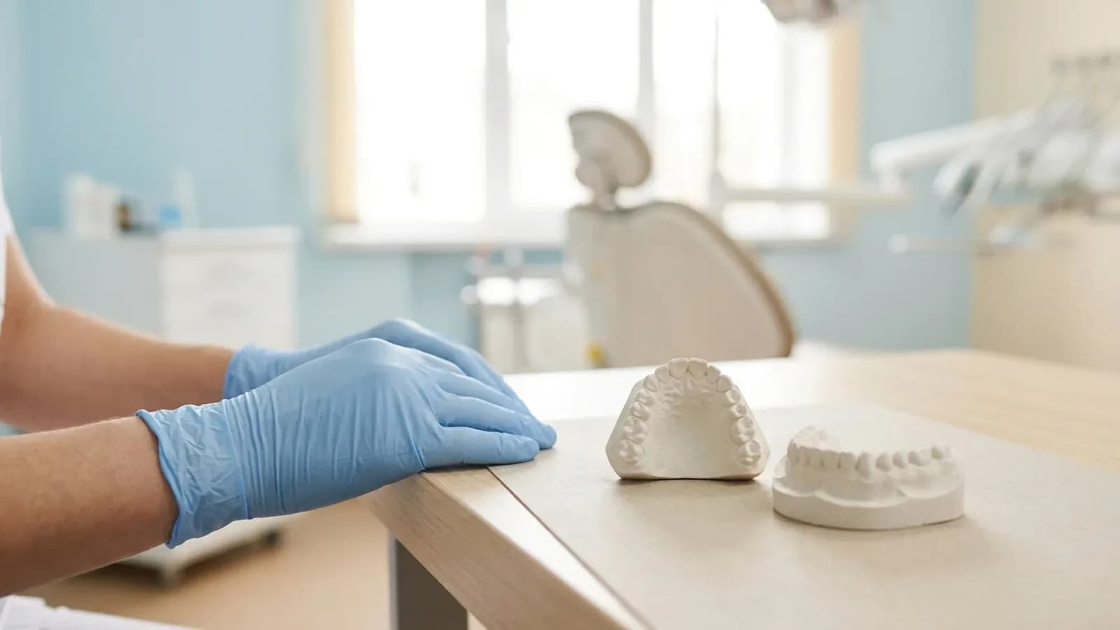 Hände in blauen Nitrilhandschuhen neben Gipsmodellen von Ober- und Unterkiefer auf einem hellen Tisch in der Praxis