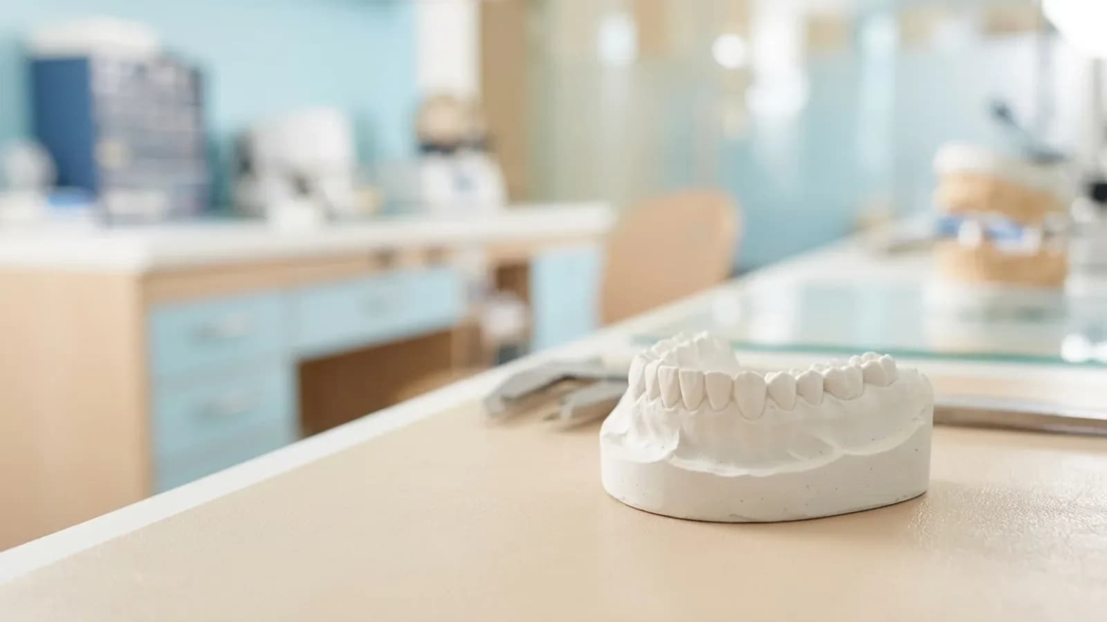 Gypsum model of a complete lower arch on a light lab bench with a softly blurred bright dental lab in the background