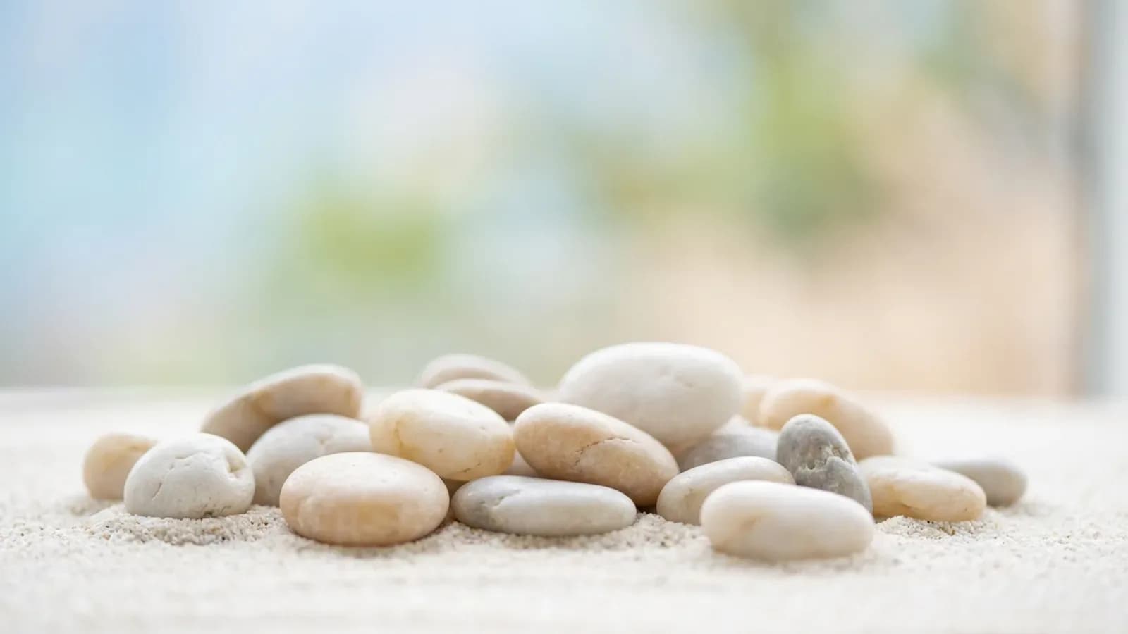 Glatt abgeschliffene helle Kieselsteine auf feinem Sand, weiches Tageslicht, unscharfer Hintergrund